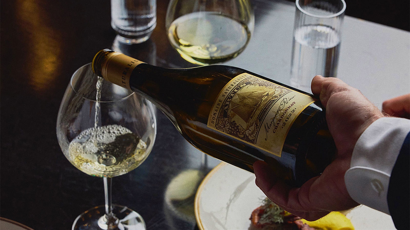 A server pouring a glass of Chardonnay next to a pasta dish